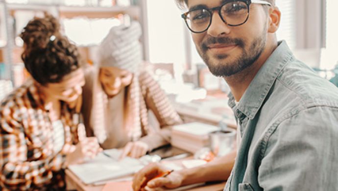 Zwei Frauen schauen auf ein Blatt, ein Mann mit Brille schaut in die Kamera
