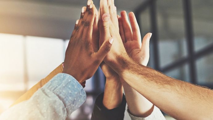 Teamwork-High-Five: Mehrere diverse Hände treffen sich zu einem gemeinsamen High-Five in einem modernen Büro mit Sonnenlicht. Symbol für Teamarbeit, Erfolg und Motivation.